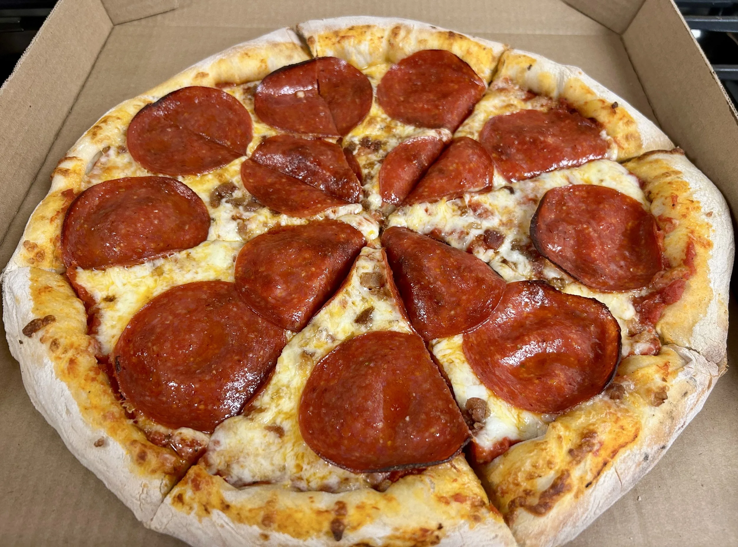 A pepperoni pizza in a cardboard box with melted cheese, tomato sauce, and crispy crust.