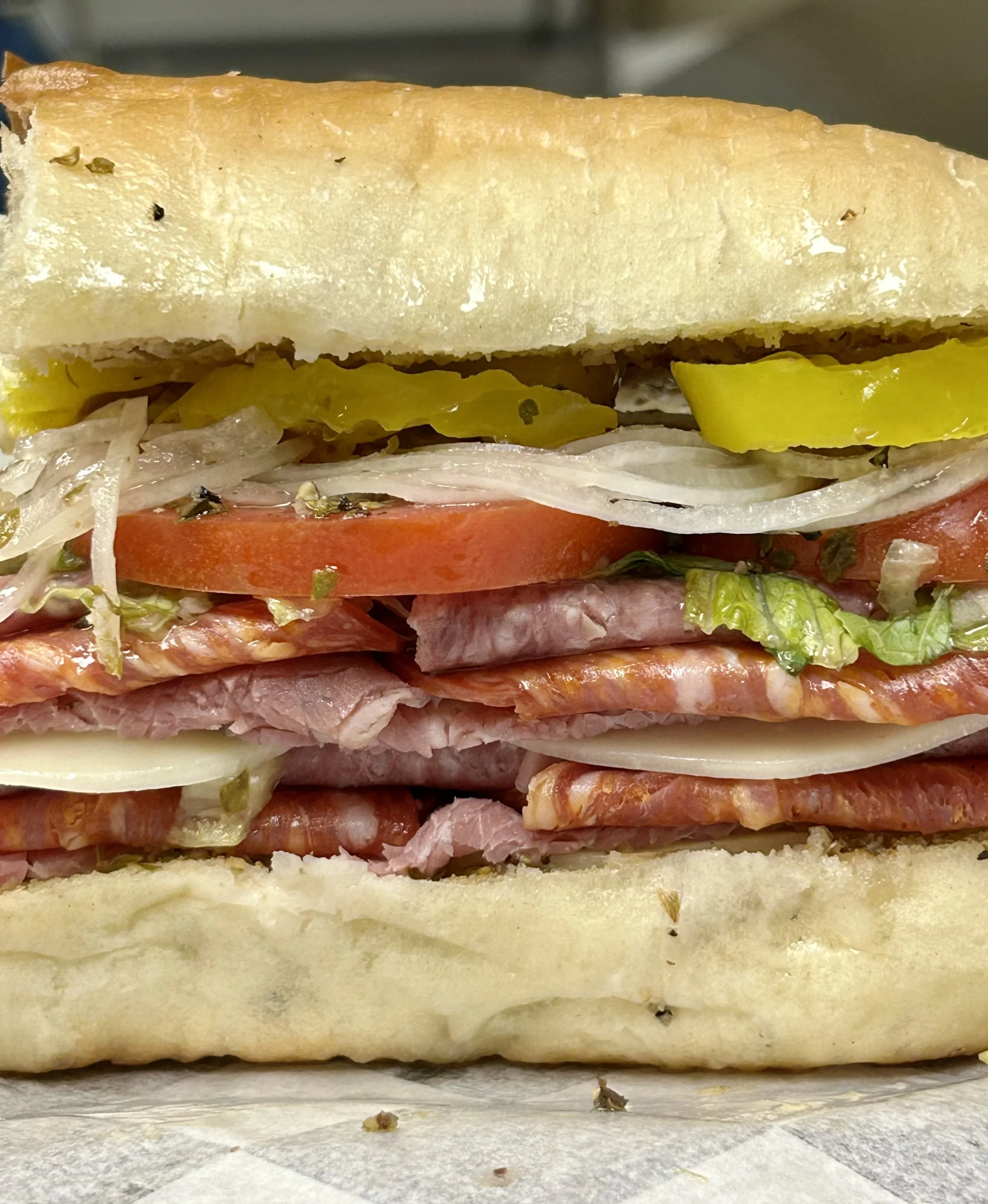 Close-up of a sub sandwich with layers of sliced meats, cheese, tomatoes, lettuce, onions, pickles, and toasted bread.