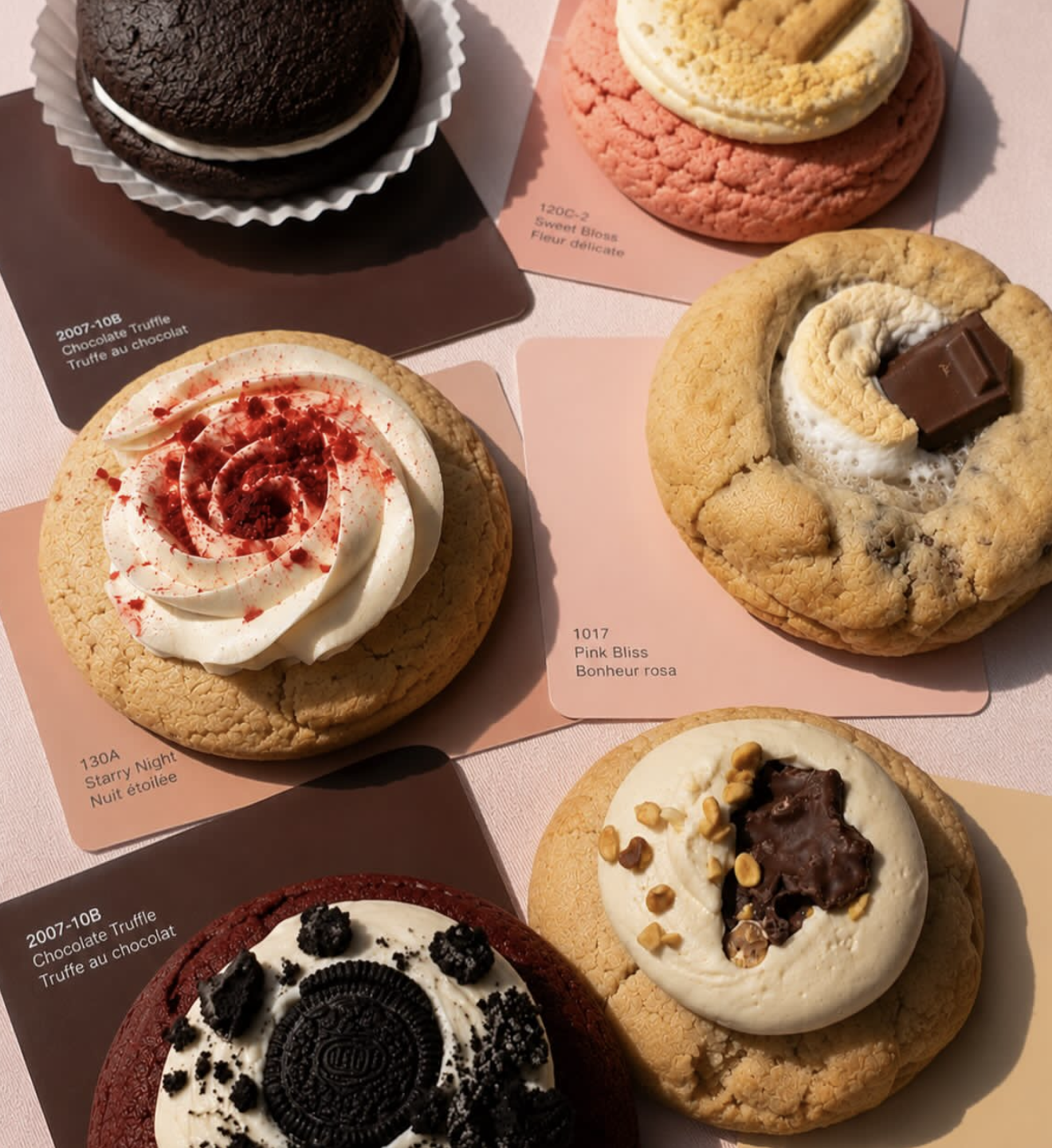 Assorted cookies on display, including one with cream and red sprinkles, one with white frosting and chopped nuts, one with chocolate chunks and cream, and one with Oreo cookies and cream.