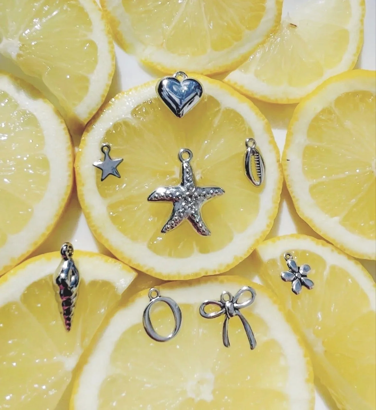 Slices of lemon with various silver charms placed on top, including a starfish, heart, flower, and other shapes.