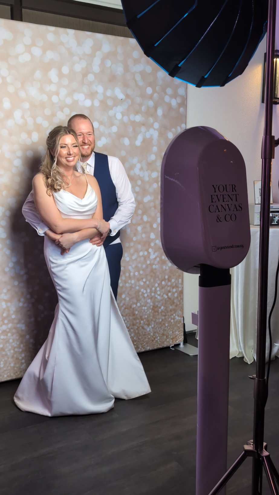 A bride and groom posing for a photo wedding photo with a sparkly backdrop and professional lighting equipment.