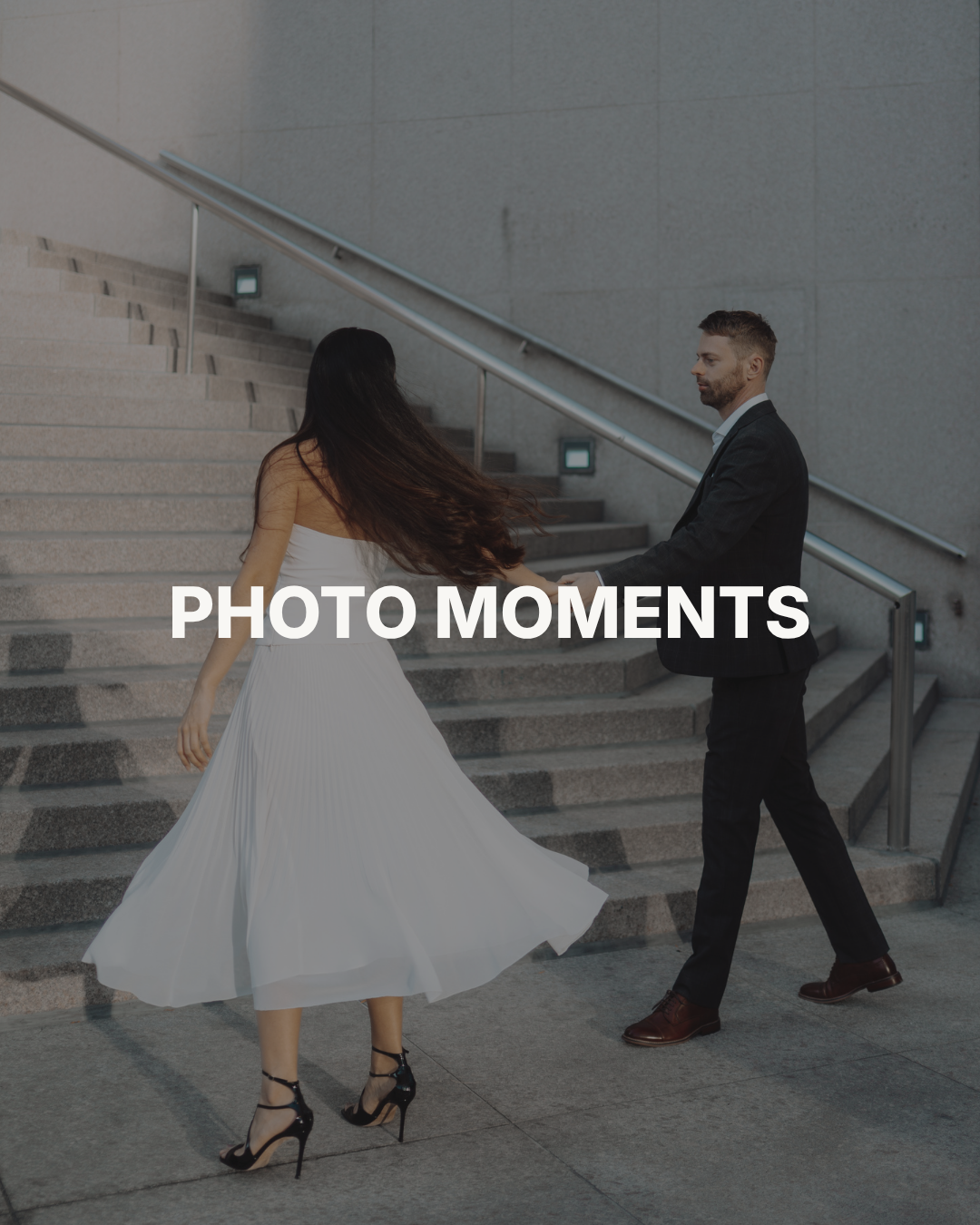 A man in a black suit holding hands with a woman in a white dress walking up stairs outside.