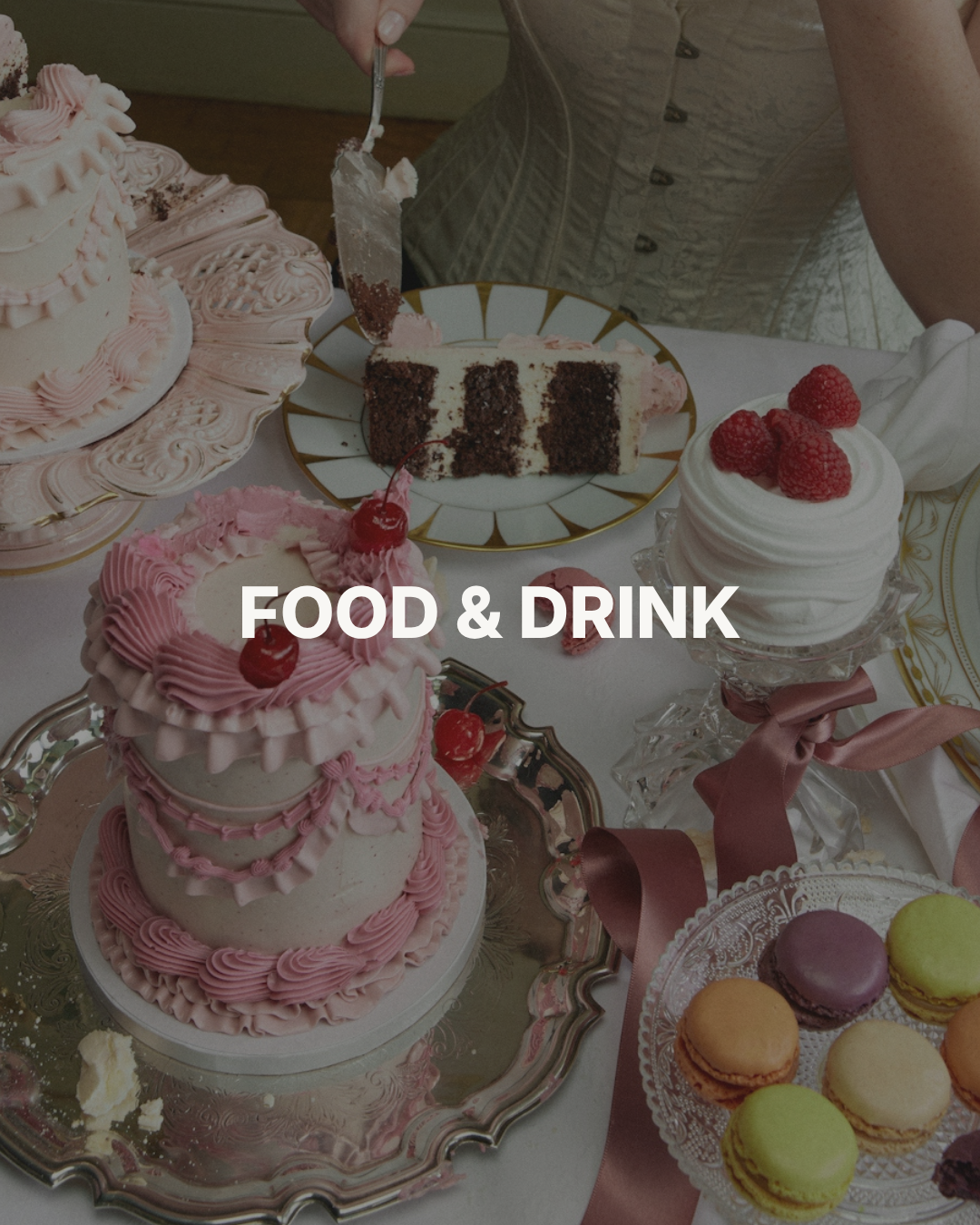 A variety of cakes and desserts on a table, including a pink layered cake with cherries, a chocolate and cream cake slice, a white frosted cake with raspberries, and a tray of colorful macarons.