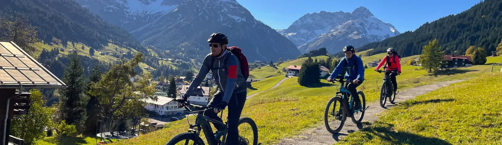 Three people riding mountain bikes on a trail through a green hillside with mountains in the background