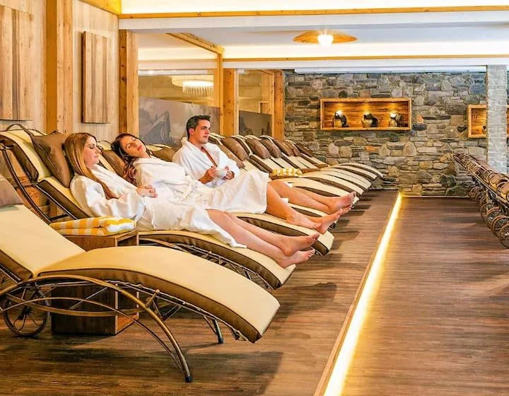 Three people lying on lounge chairs with white towels in a spa lounge area.