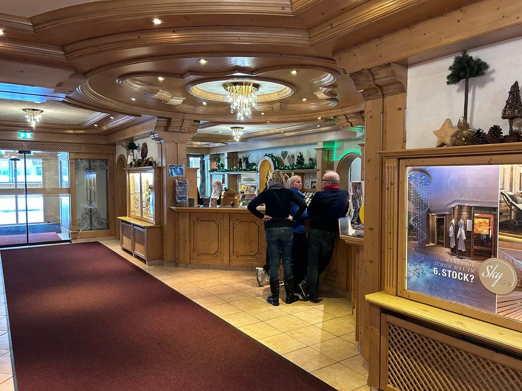Lobby with wooden decor, reception desk with three people talking, Christmas decorations, a fire image in a poster, and entrance doors.