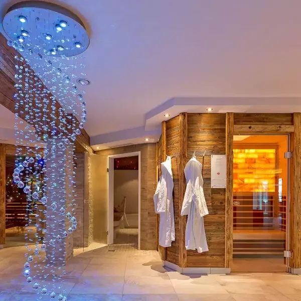 Luxury spa room with wooden walls, a hanging bubble shower, and white robes on hooks.