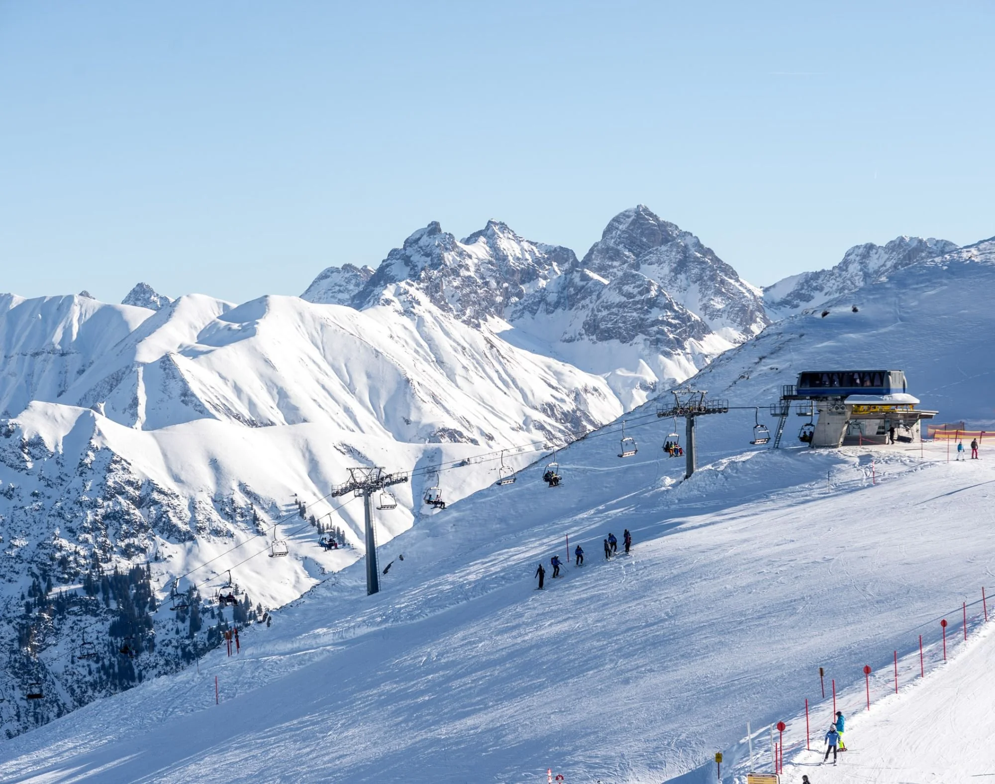 Snow-covered mountains with ski lifts and skiers on a sunny day at a ski resort.