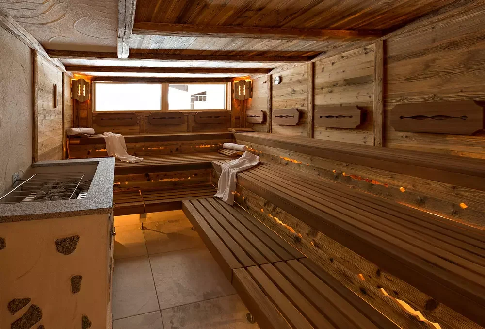 A cozy indoor sauna with wooden benches, a towel, and a small heater in the corner, illuminated with warm lighting.