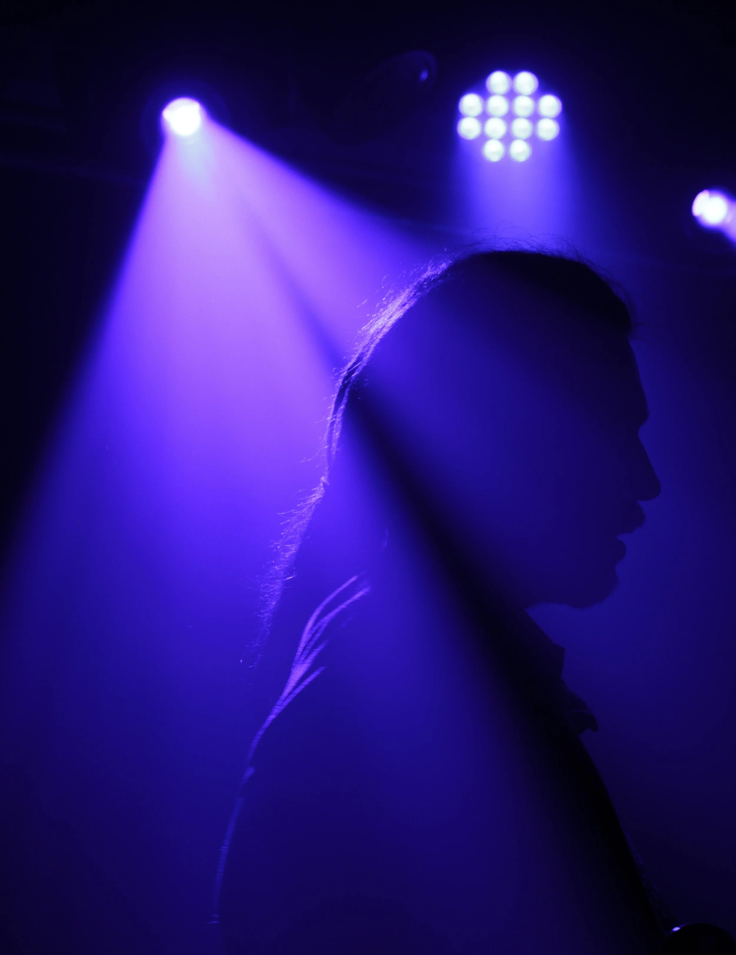 Silhouette of a person's head and shoulders against a dark background with blue stage lights