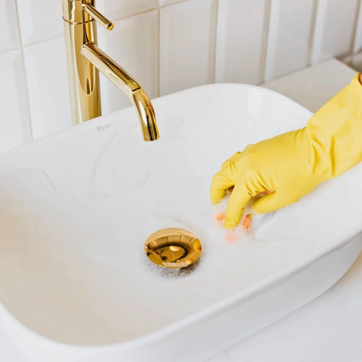 Person wearing yellow gloves cleaning a white sink with a pink scrub brush.