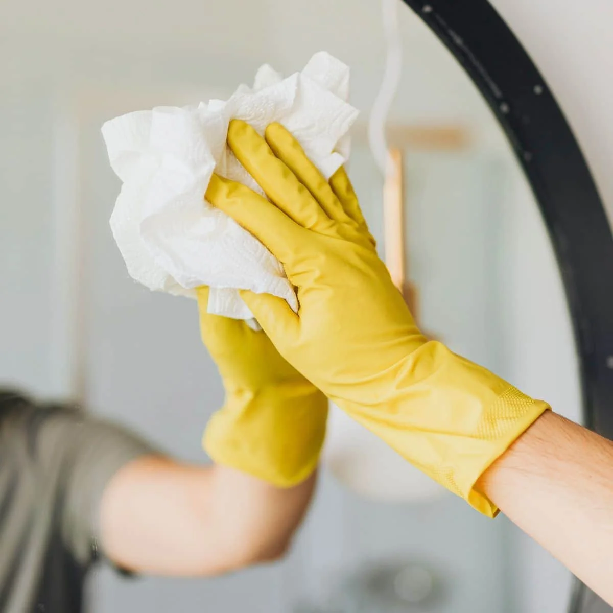 Person wearing yellow rubber gloves cleaning a glass surface with a cloth.