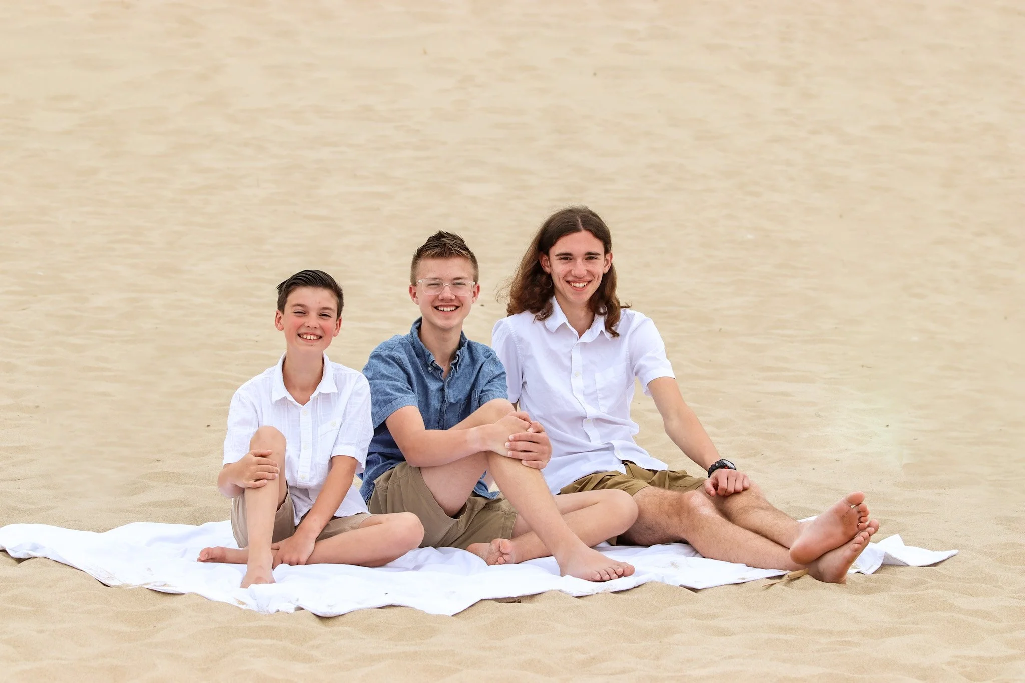 Three boys sitting on a white blanket on the sand at the beach. family photo, beach, west michigan
