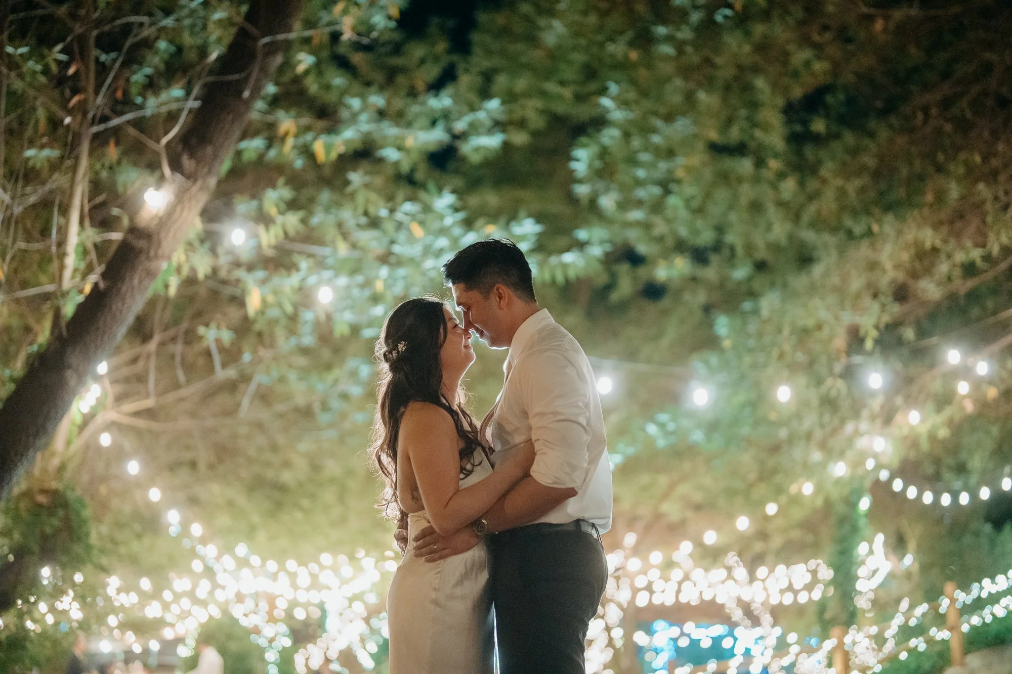 Couple kissing under glowing string lights at night