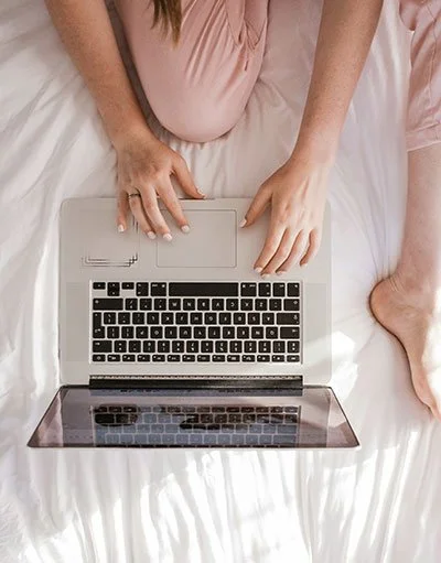 Person sitting on a bed using a laptop with a black keyboard.