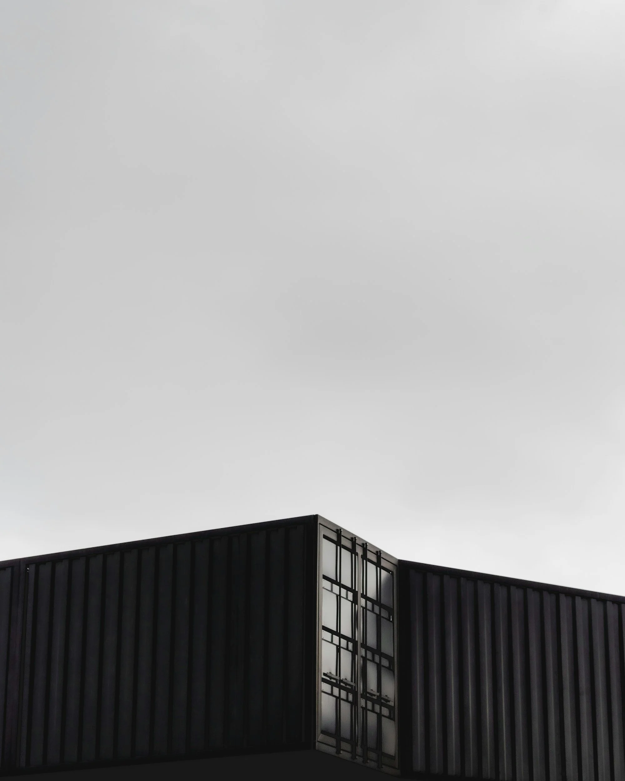 Close-up of a modern black building with metal siding and a large window on a cloudy sky background.