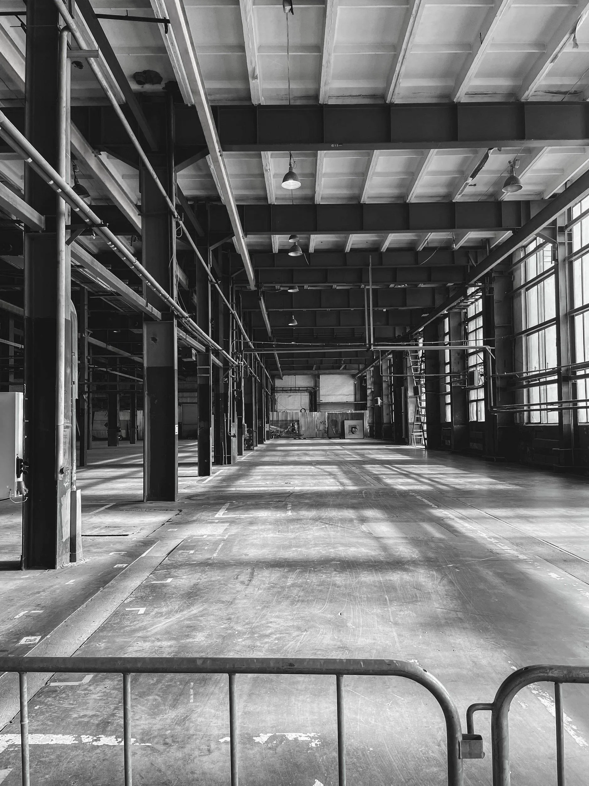Empty industrial warehouse or factory with large windows, metal beams, and a high ceiling, black and white photo.