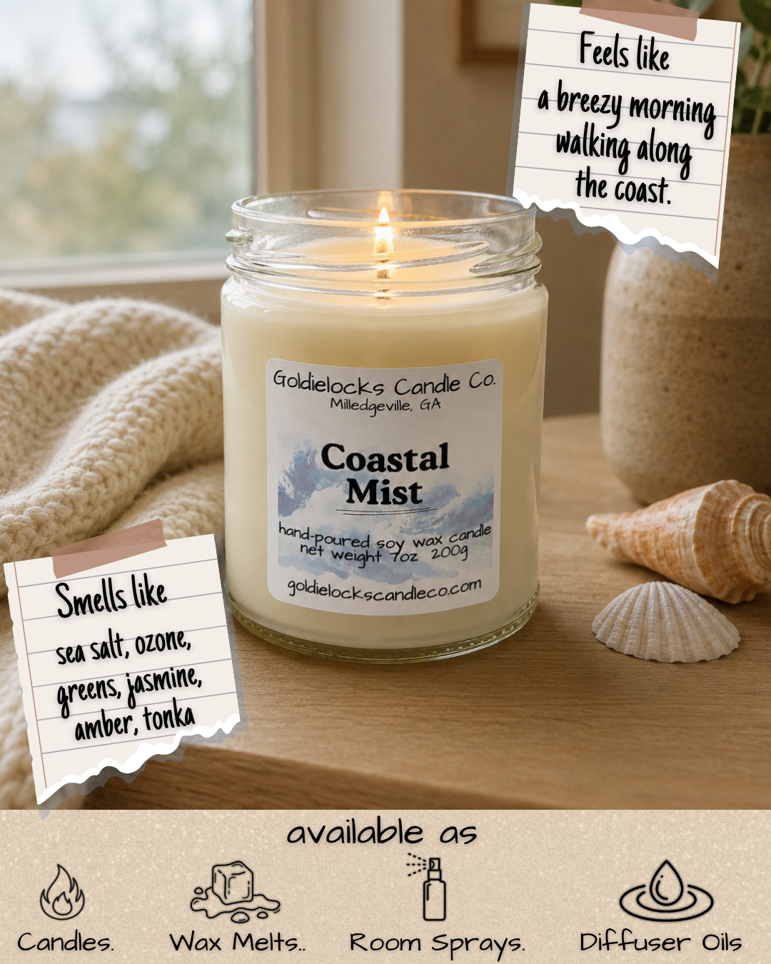 A lit Coastal Mist scented candle from Goldielocks Candle Co. on a wooden surface decorated with seashells, with notes indicating it smells like sea salt, ozone, greens, jasmine, amber, and tonka, and feels like a breezy morning walking along the coast.