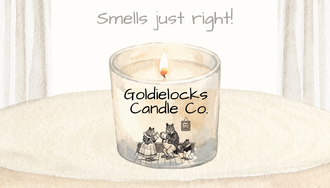 A lit candle with floral designs and the text 'Goldielocks Candle Co.' on it, placed on a surface with a textured background.