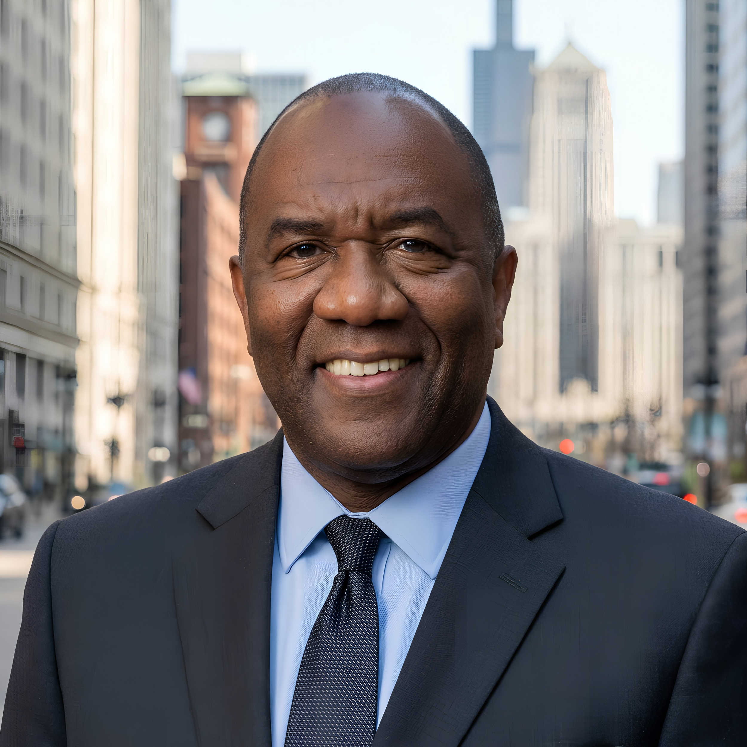 A man in a suit smiling, with a cityscape of tall buildings and skyscrapers in the background.
