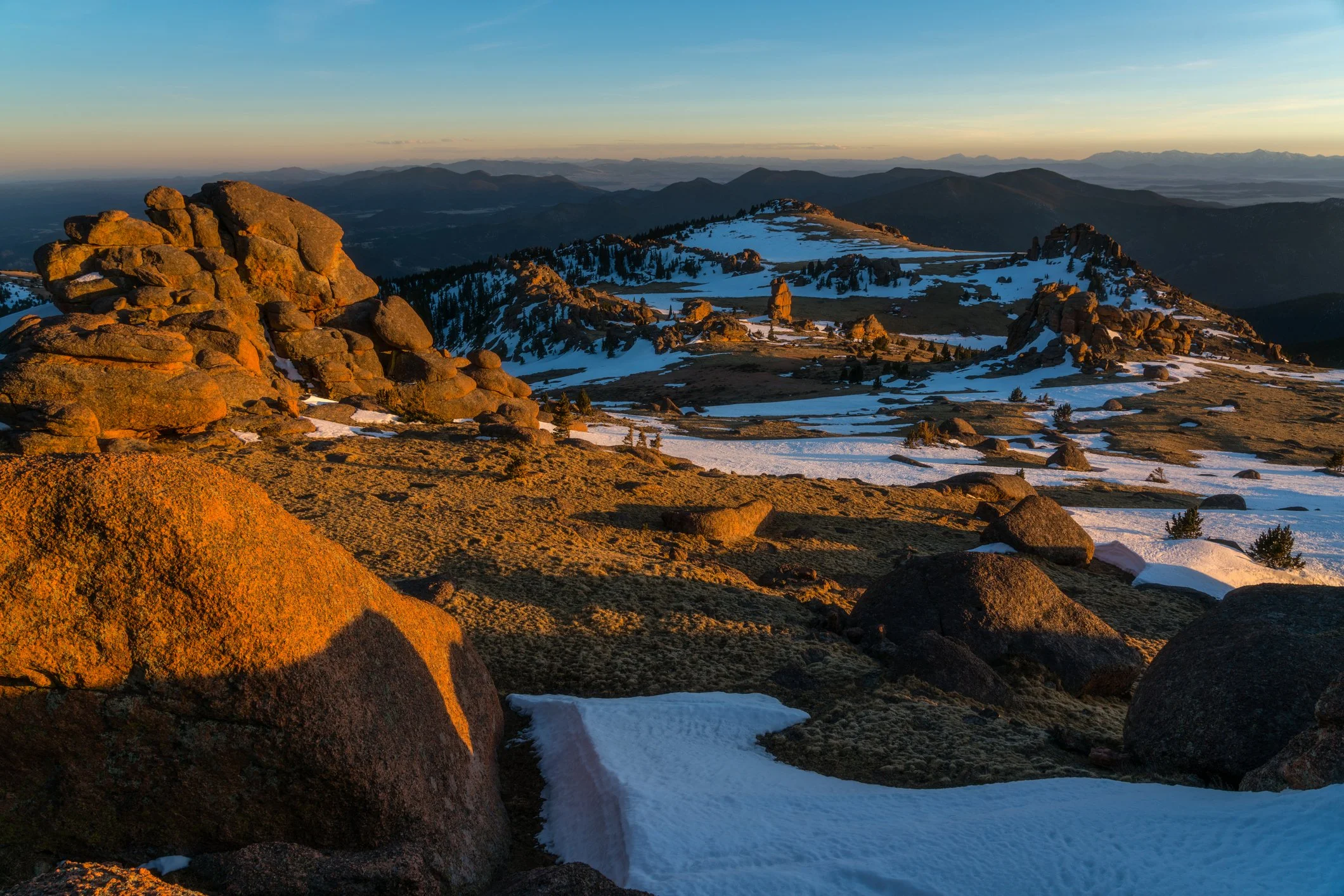Sunset over mountain landscape with rocks and patches of snow.