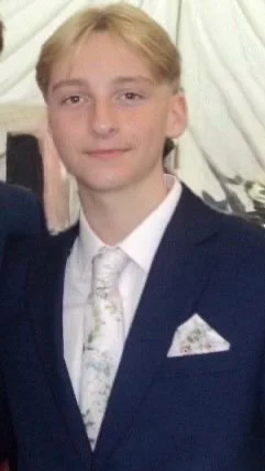 Young man in a formal suit and tie, smiling, standing indoors.