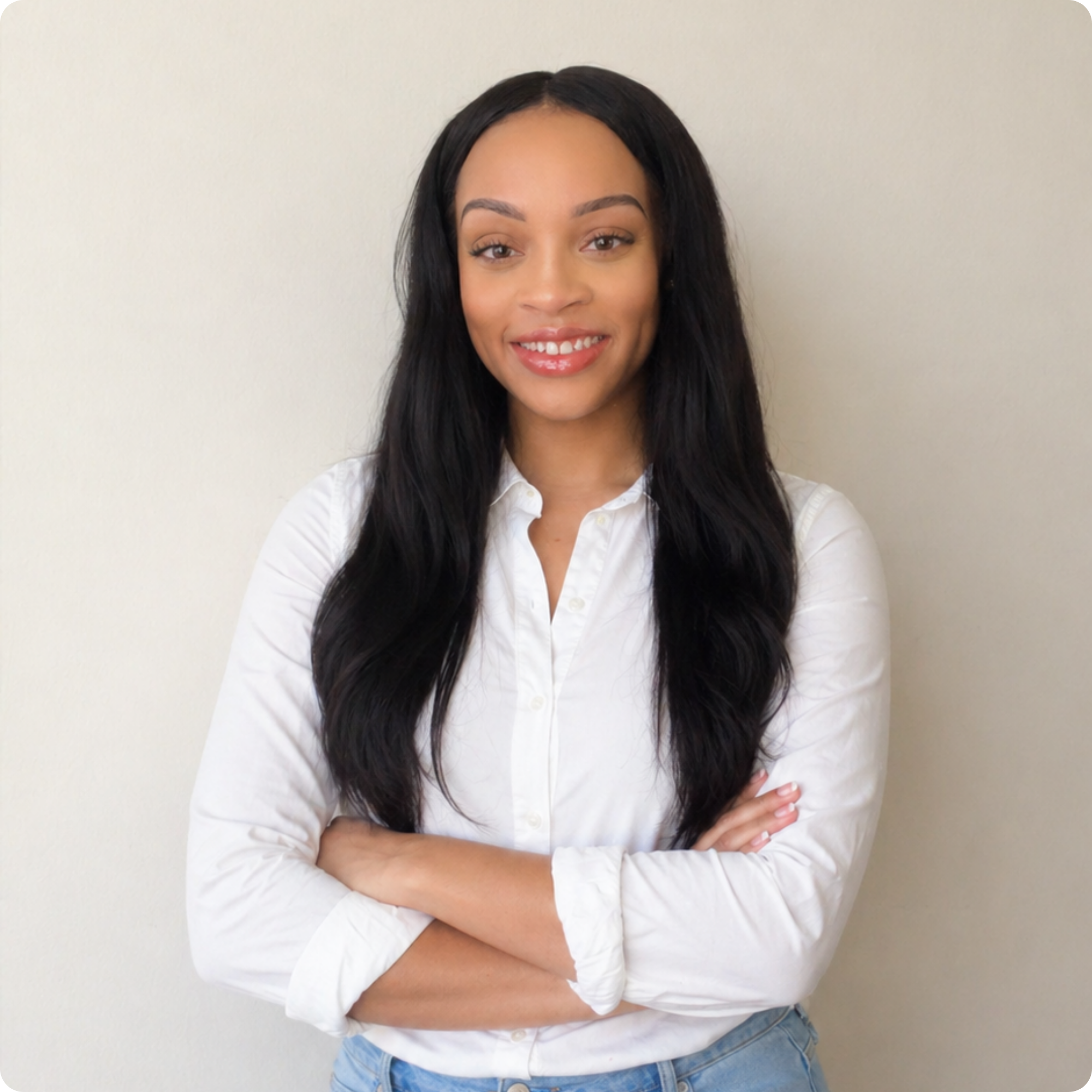 A woman with long black hair, wearing a white shirt and blue jeans, standing against a plain light-colored wall.