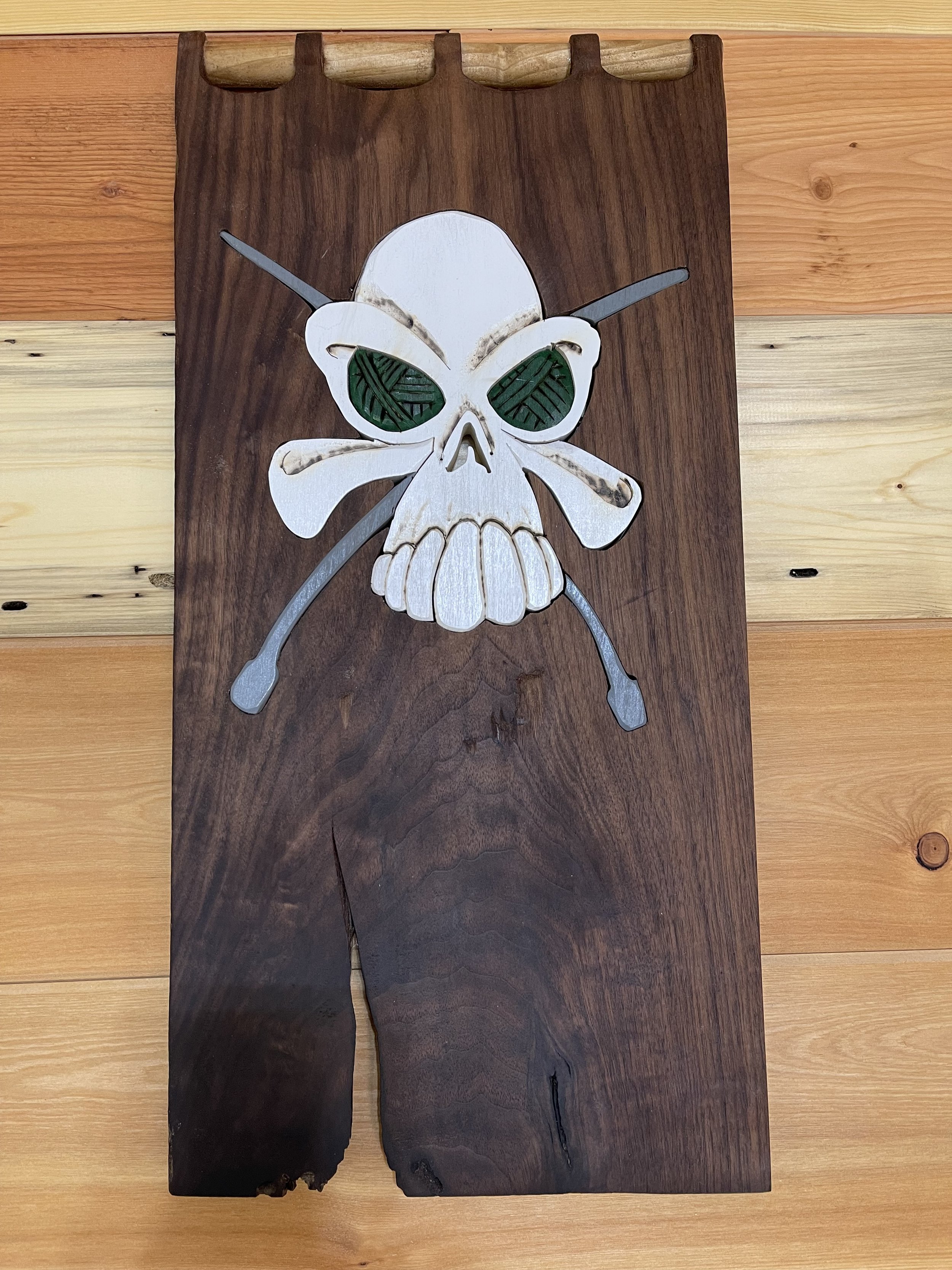 Wooden wall art featuring a skull with green leaf-patterned eyes and butterfly wings, with metal sticks crossing behind it.