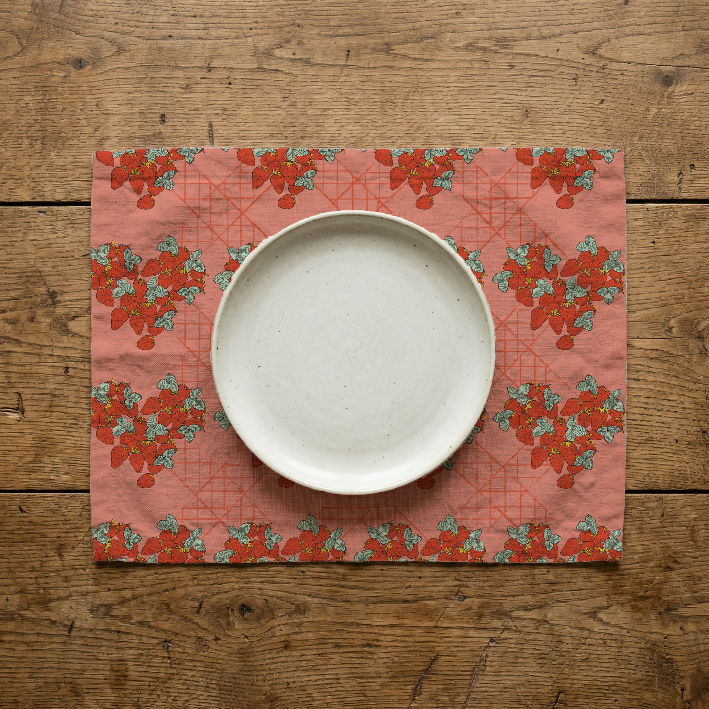 Top view of a white bowl on a pink and red strawberry-themed placemat on a wooden table.