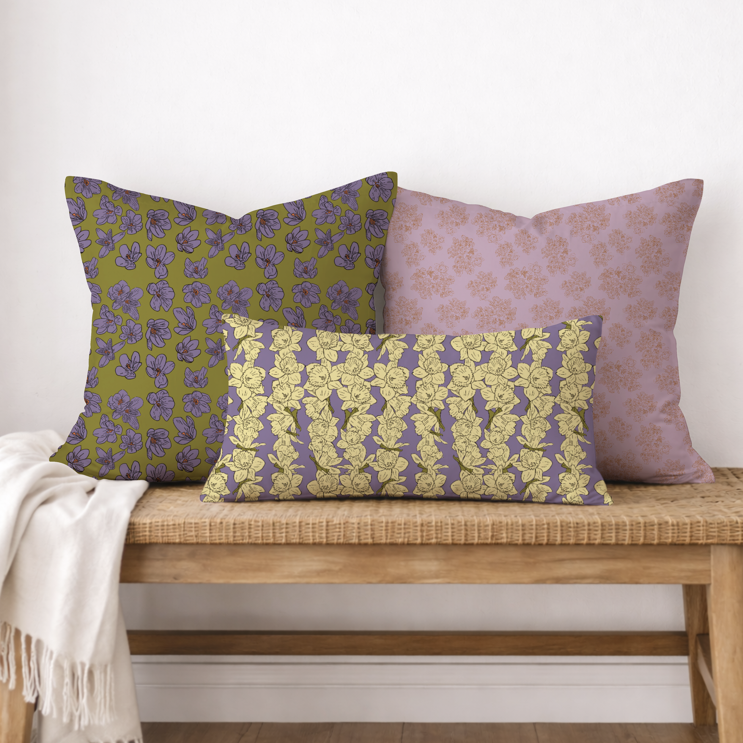 Three decorative pillows with floral patterns on a wooden surface, with a white blanket partially draped over the edge of the surface.
