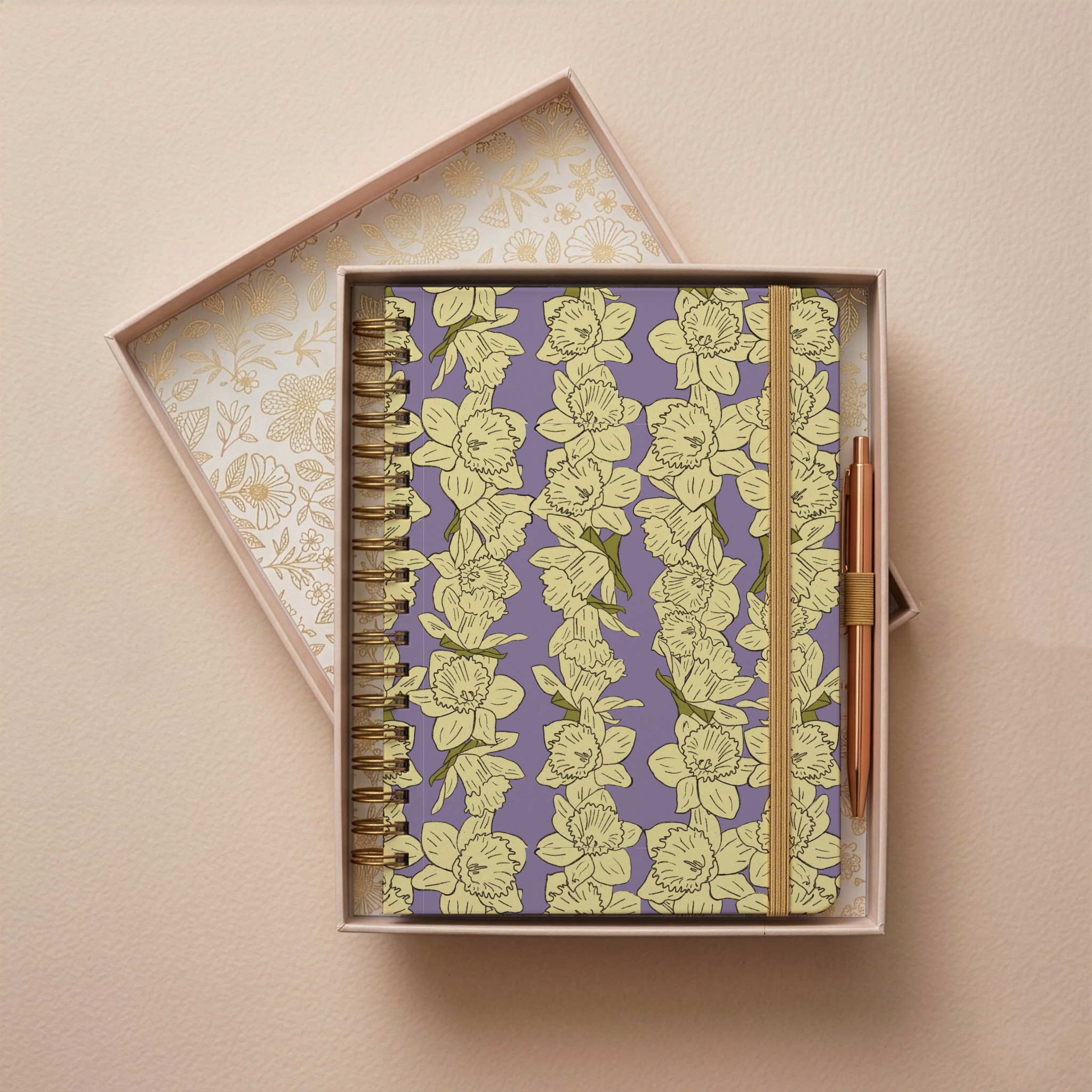 A floral patterned planner with yellow flowers and green leaves on a purple background, placed inside a decorative box with gold floral lining, on a beige wall.