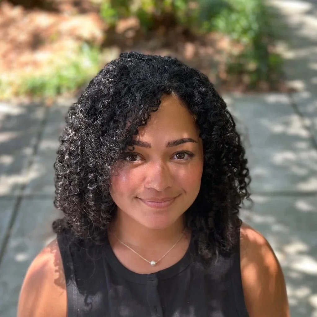 A young woman with curly black hair smiling outdoors.