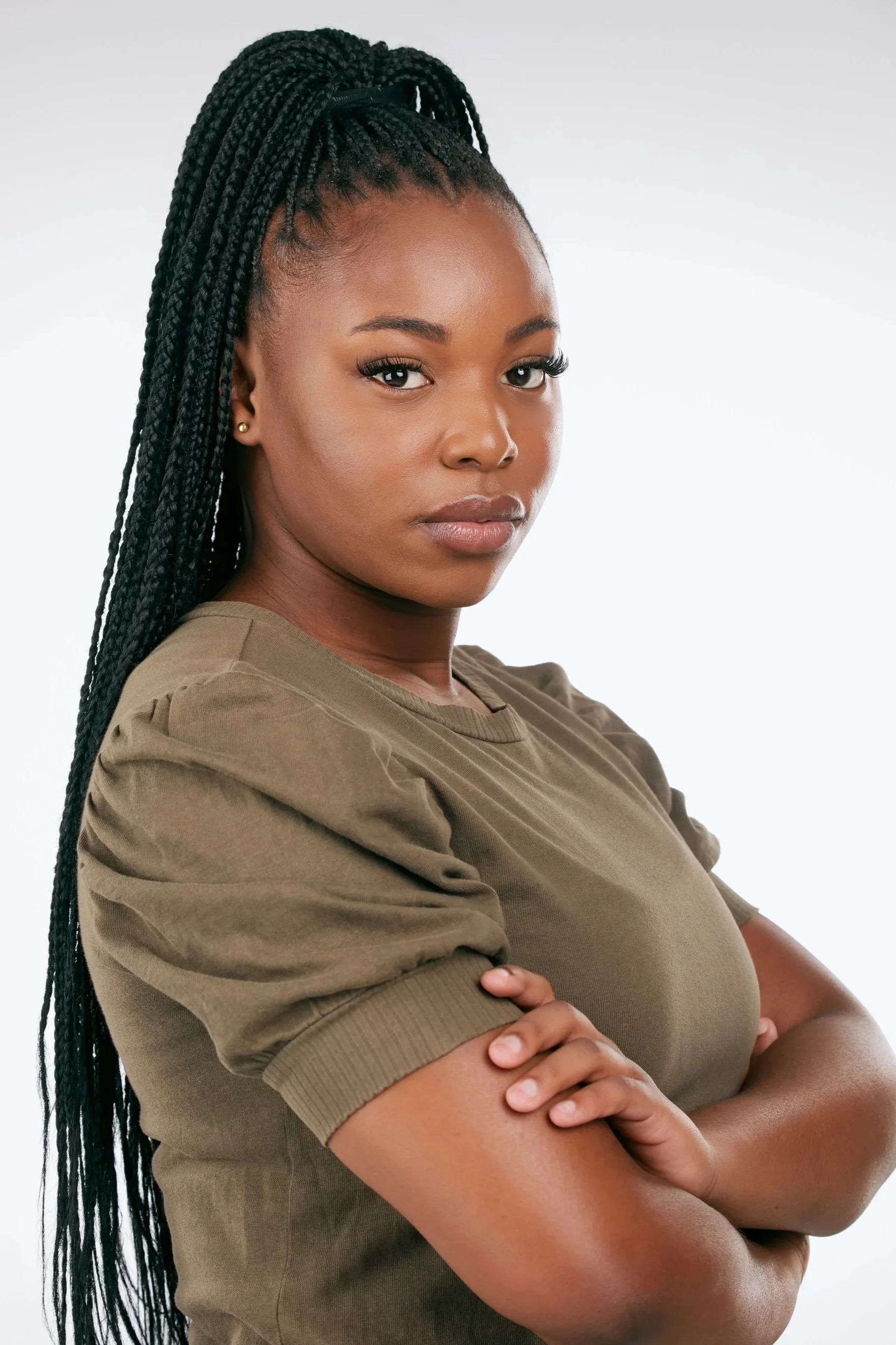 Portrait of a woman with long braided hair, wearing a brown shirt with rolled sleeves, standing with her arms crossed, looking confidently at the camera.