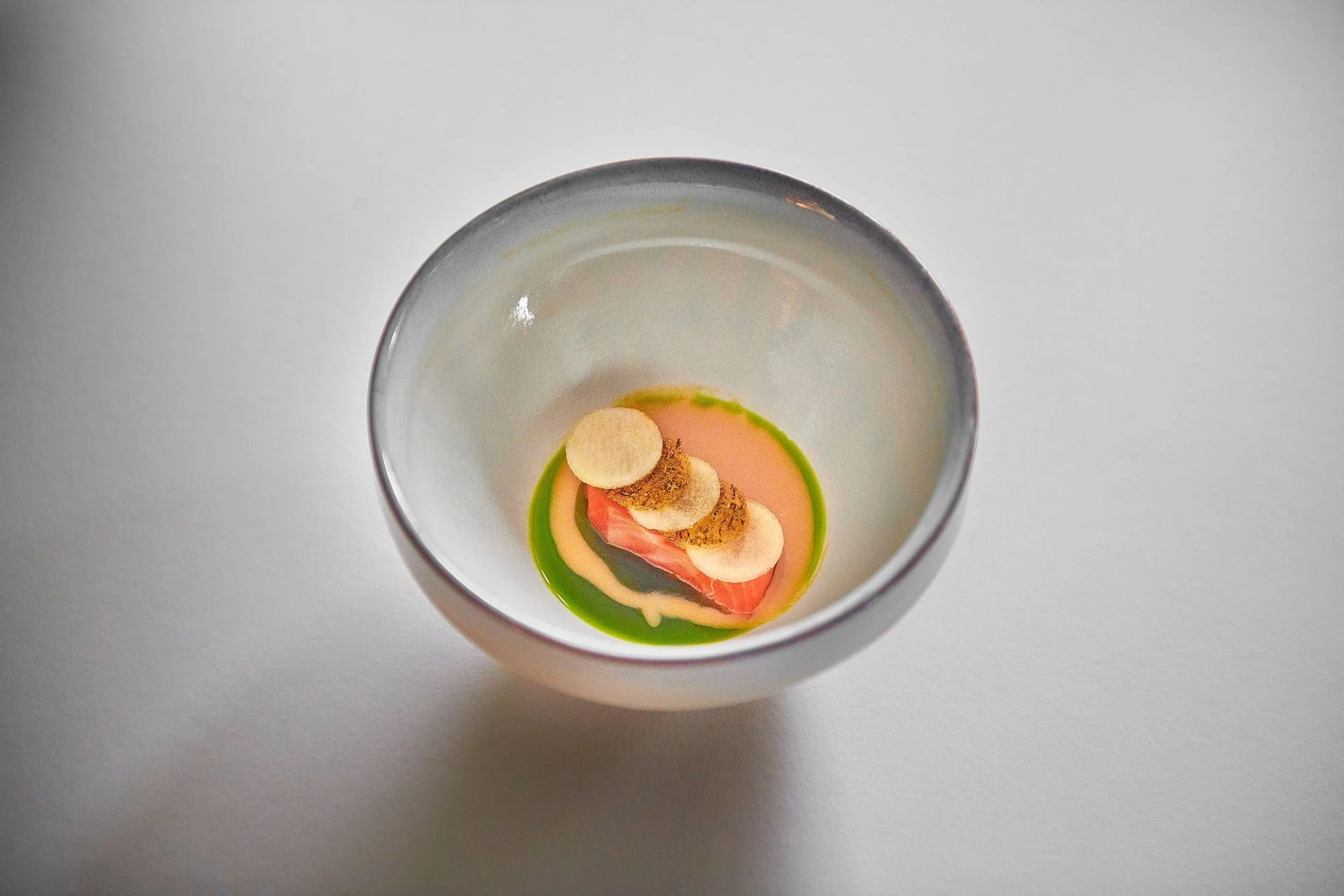 Kleines Gourmet-Gericht in einer weißen Schale, mit rotem Fisch, grüner Sauce, cremiger Sauce und kleinen Brownies