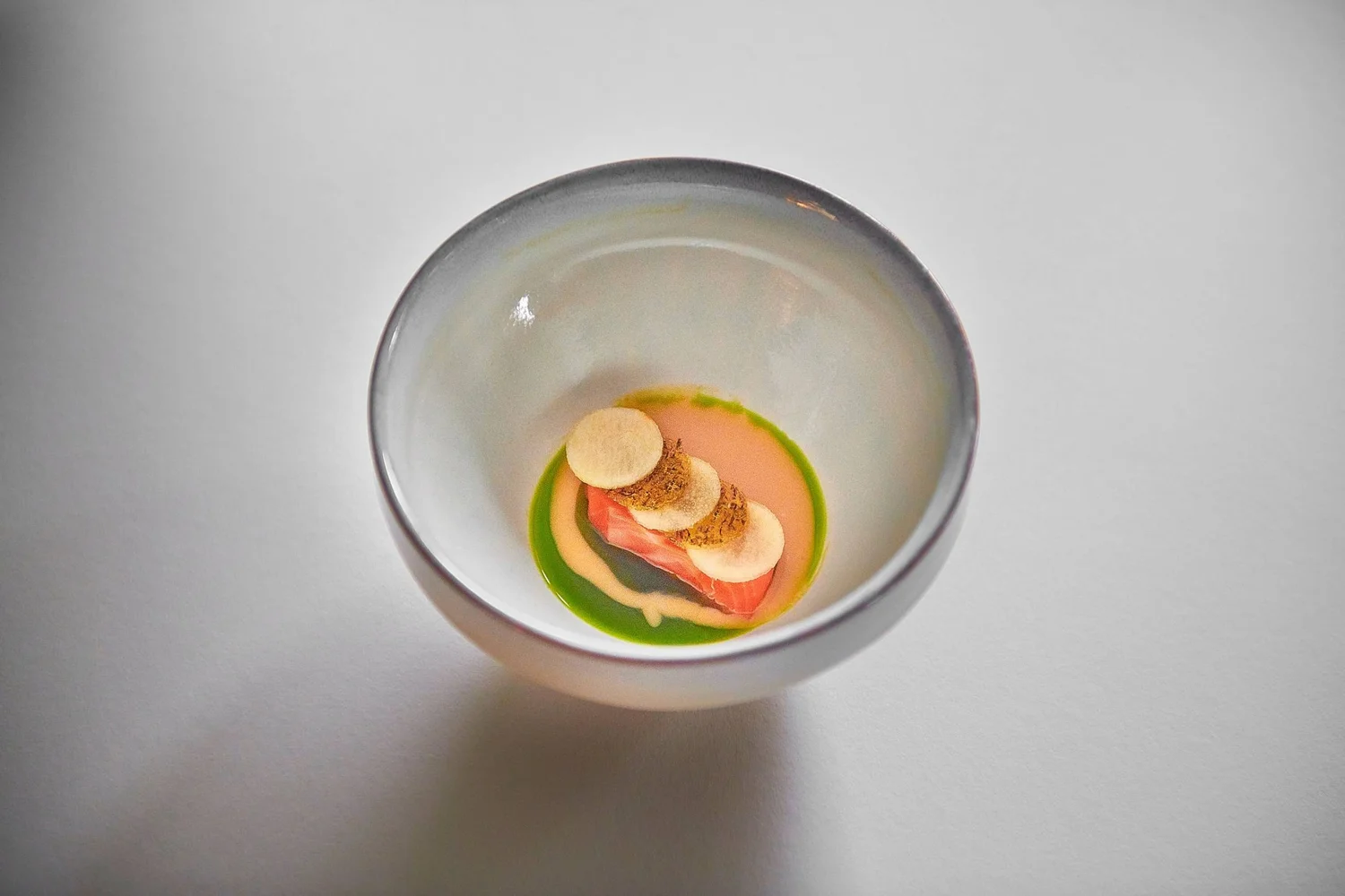 Kleines Gourmet-Gericht in einer weißen Schale, mit rotem Fisch, grüner Sauce, cremiger Sauce und kleinen Brownies