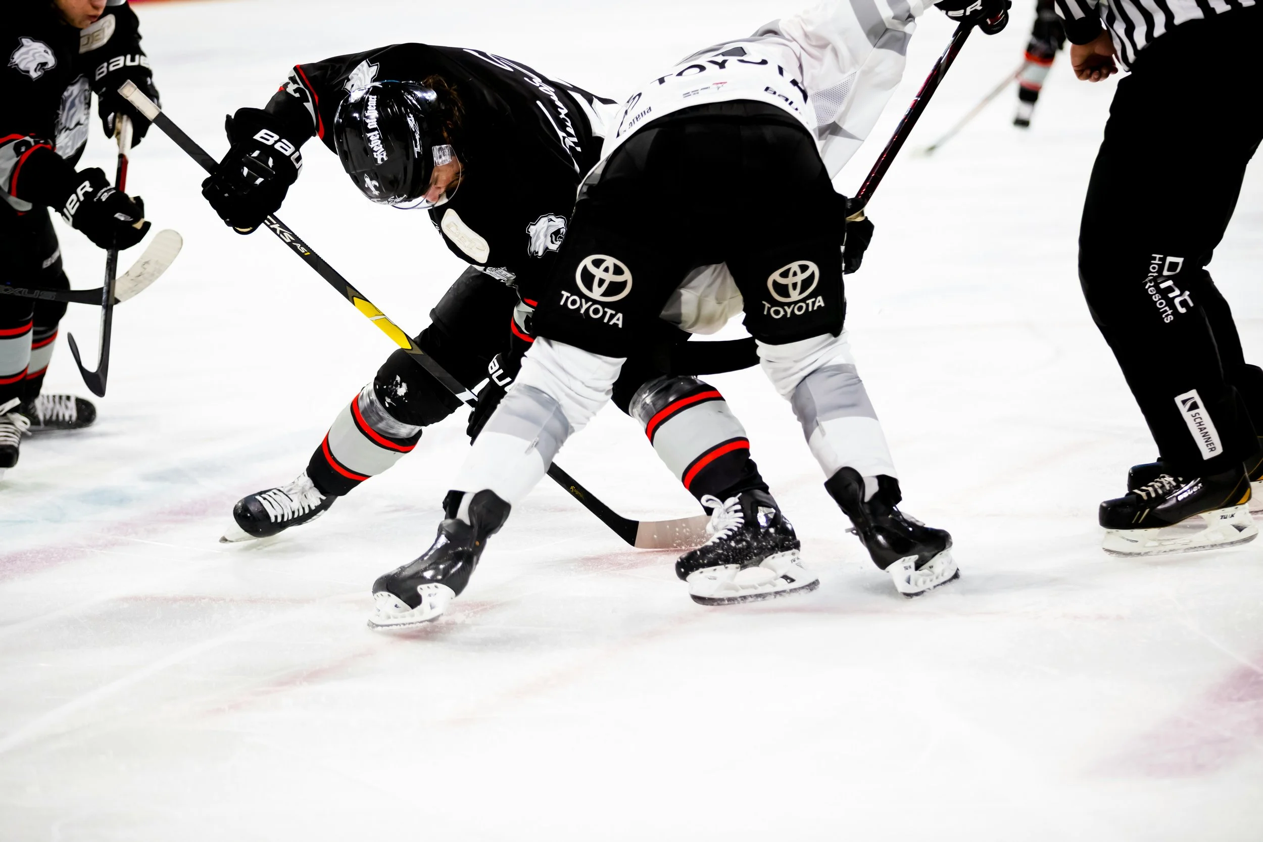 Hockey players wearing black and white jerseys with Toyota logos competing for the puck on an ice rink.