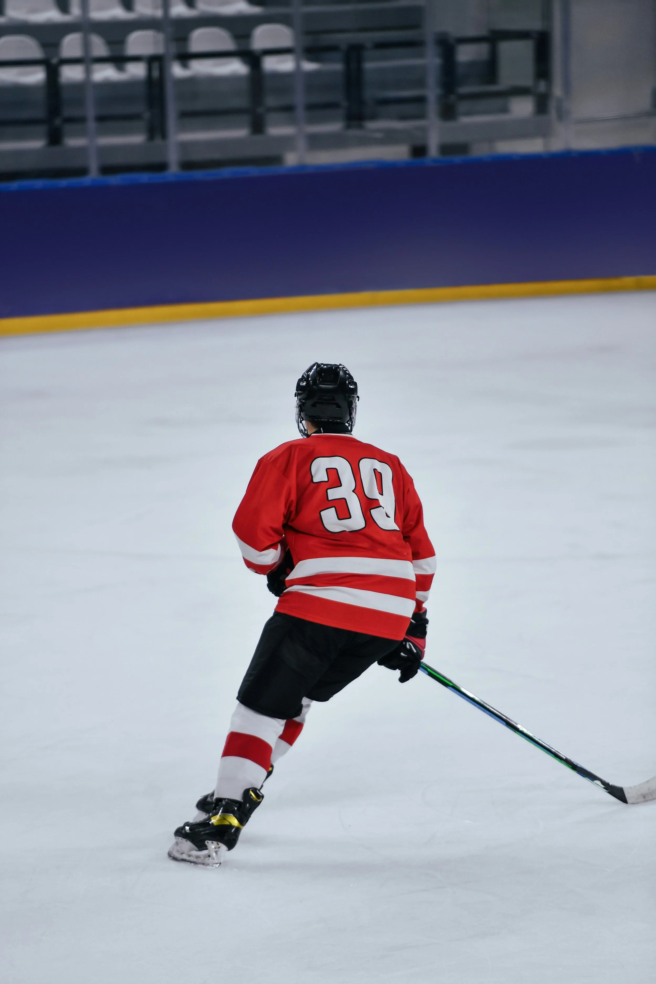 Hockey player wearing a red jersey with the number 39, skating on ice in an indoor rink.
