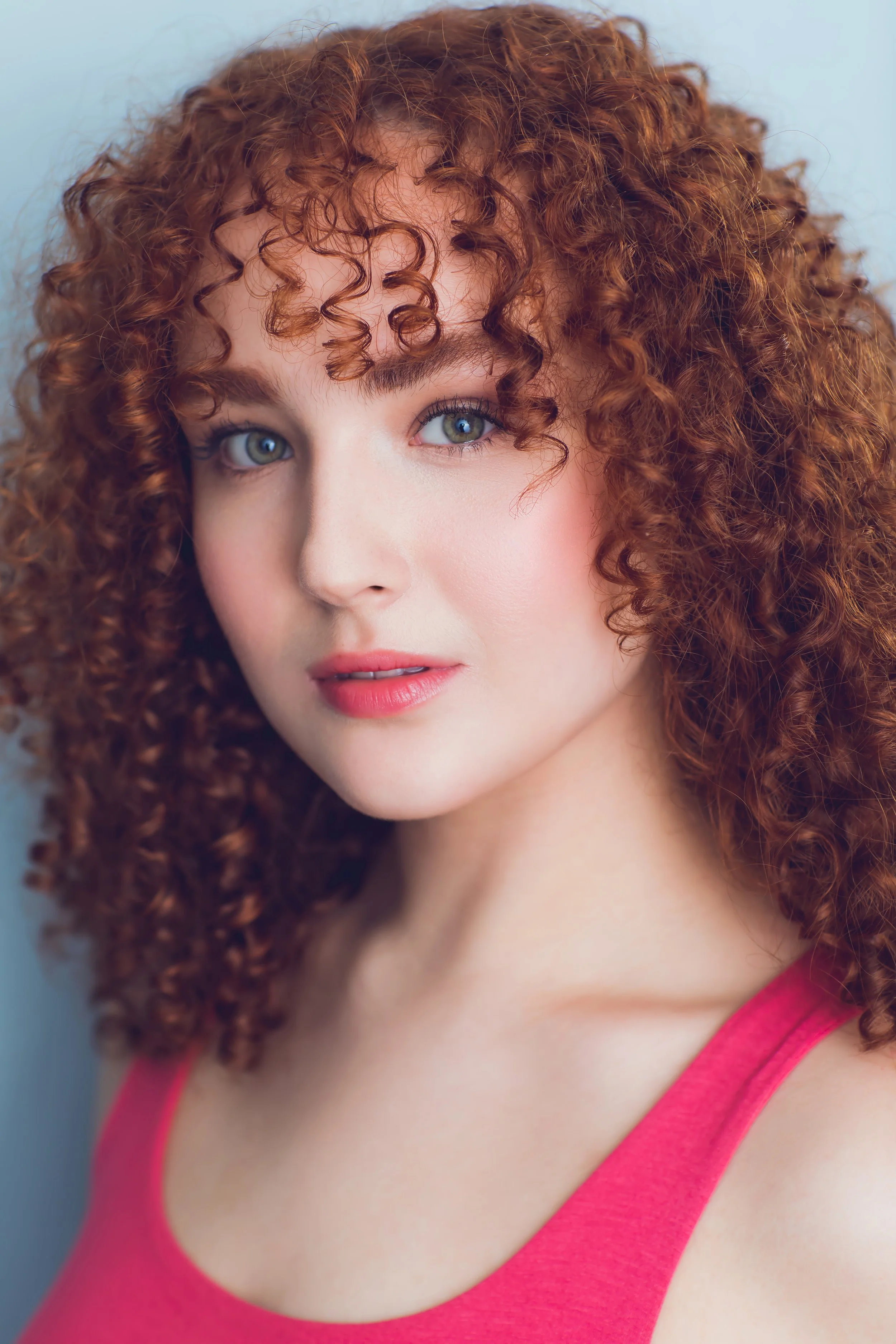 Close-up of a woman with curly red hair wearing a pink top.