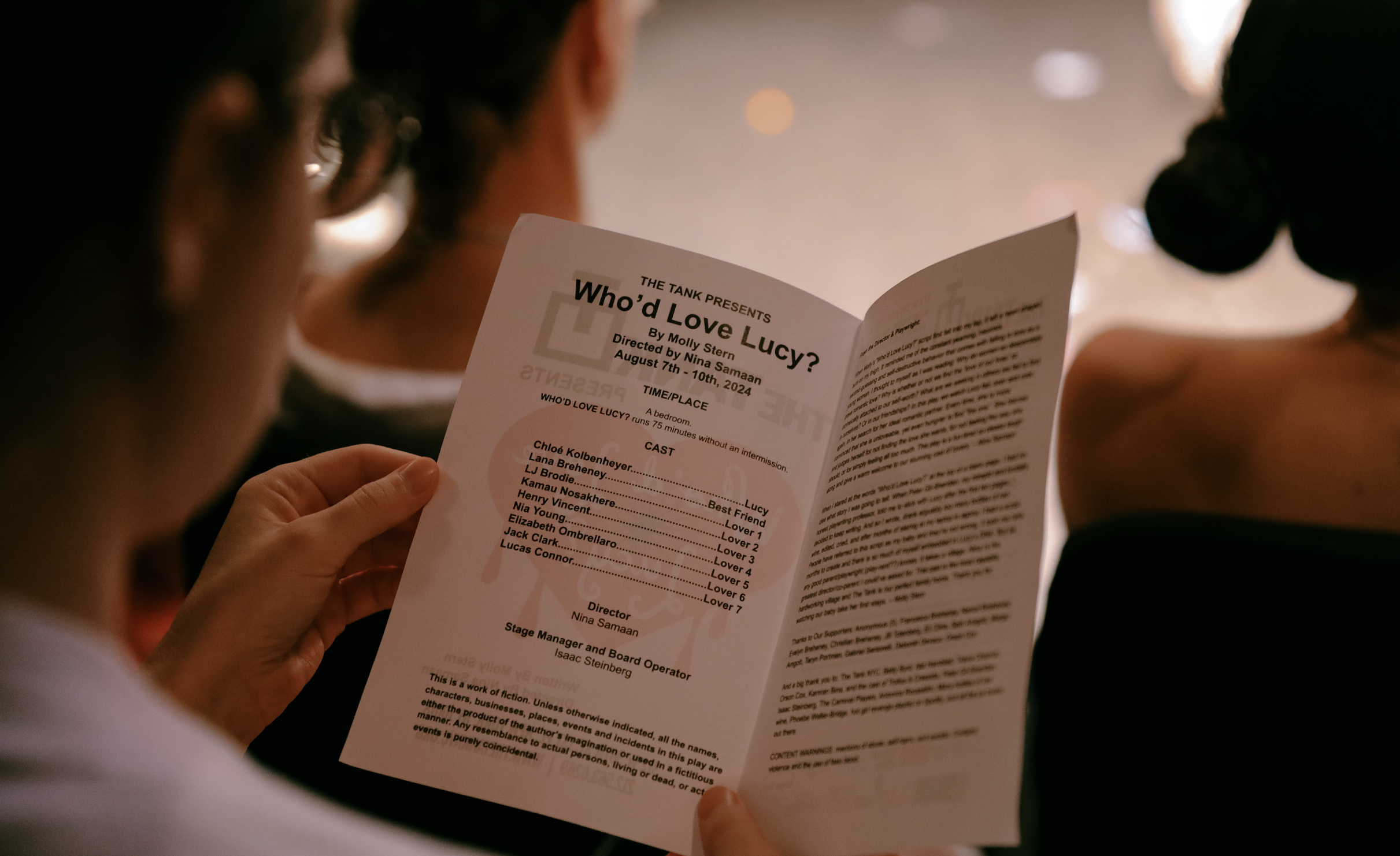 A person is holding a playbill for a theatrical production called 'Who'd Love Lucy?' with the cast and crew listed on the inside page.