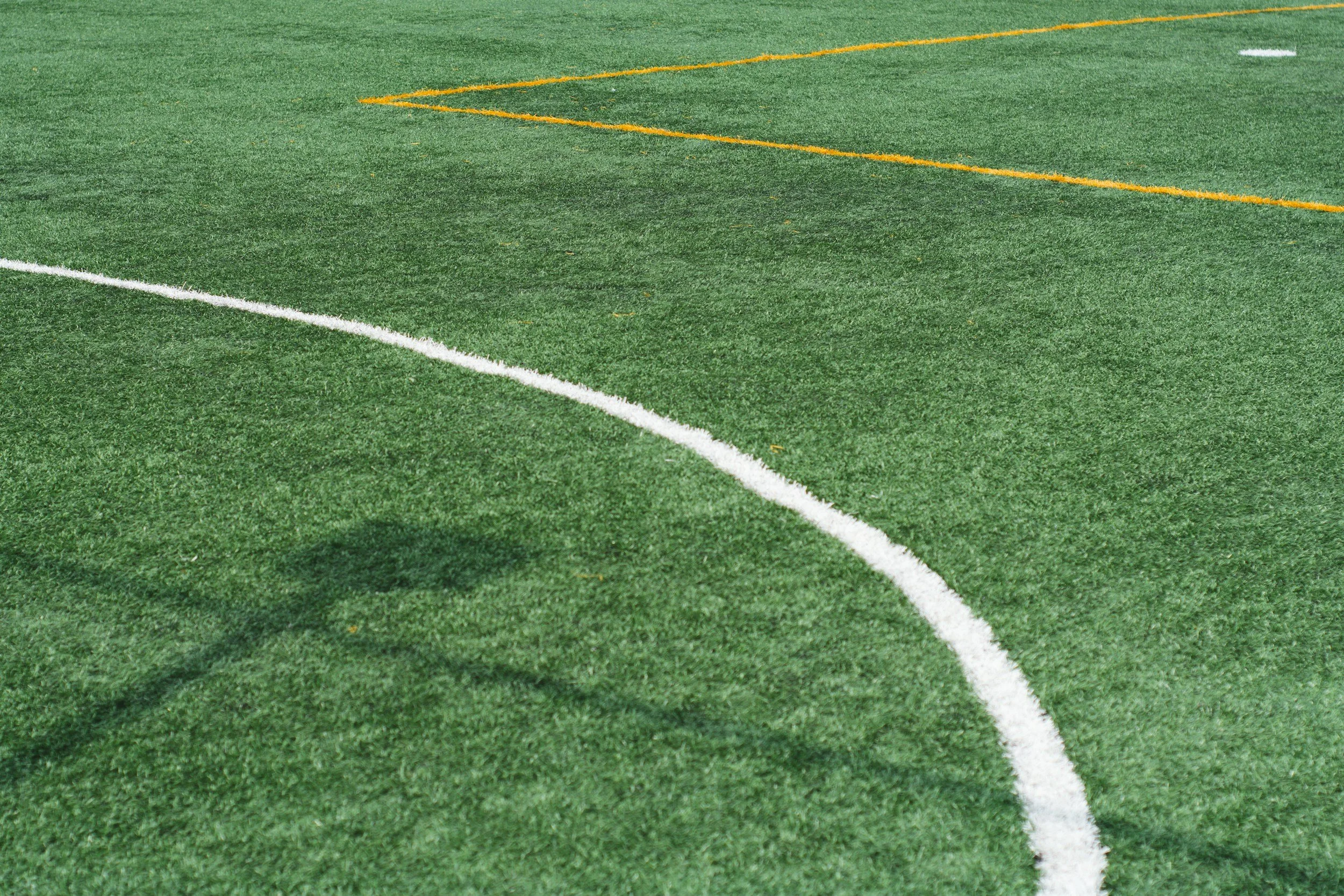 Close-up of a green sports field with white and yellow boundary lines.