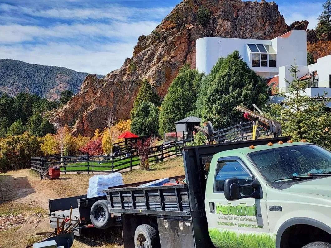 A landscape scene with a white modern building on a hillside, surrounded by trees and colorful foliage, with a pickup truck parked in the foreground.