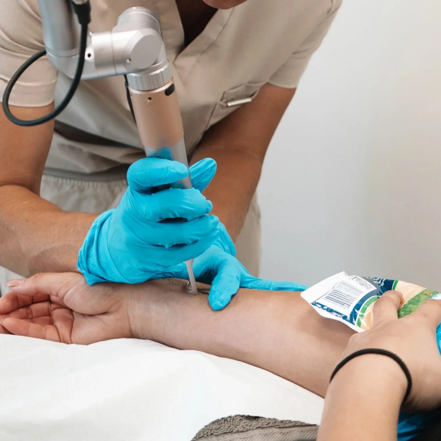 A healthcare professional in blue gloves drawing blood from a patient's arm with a syringe, while the patient holds a colorful packet.