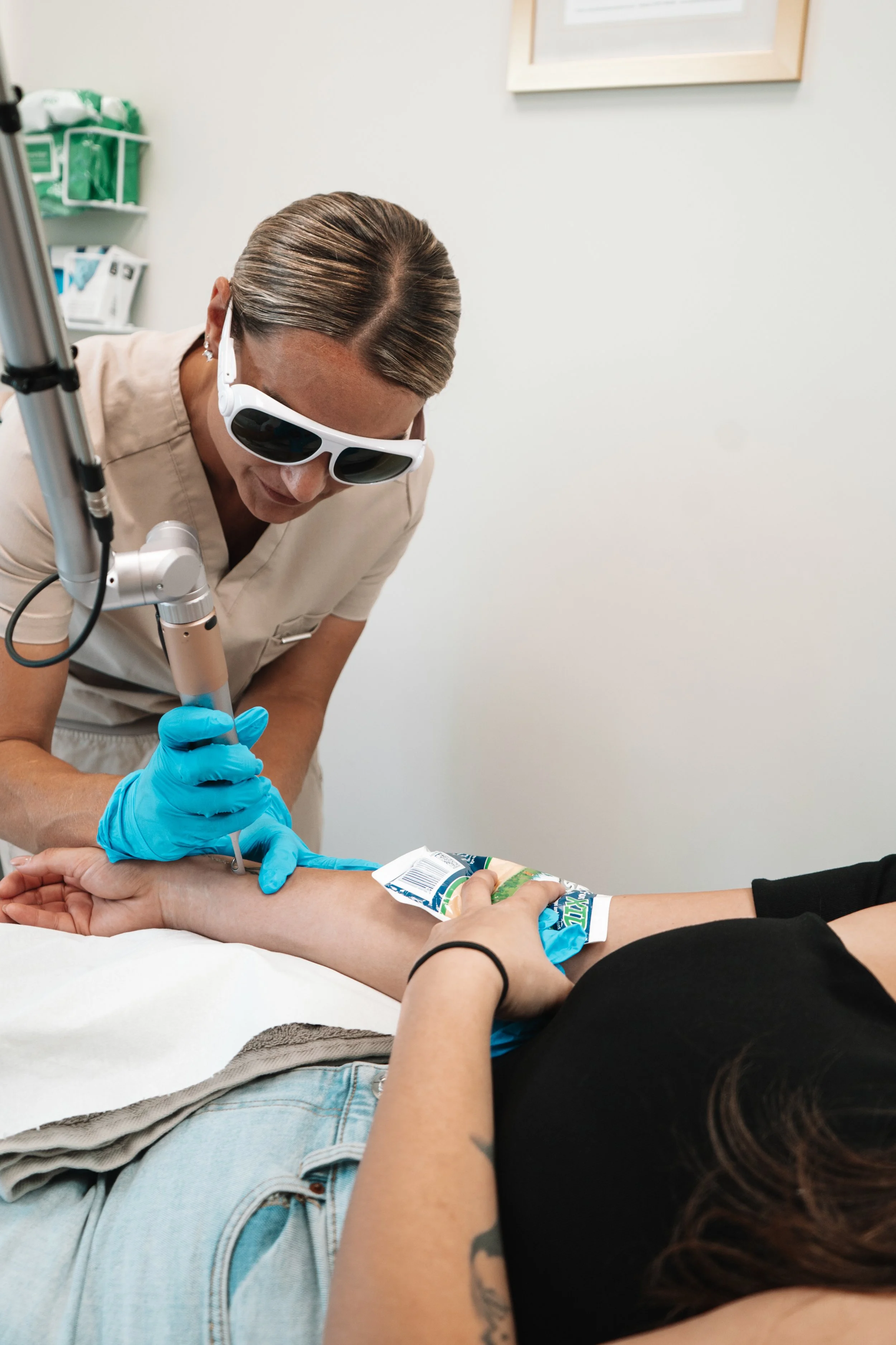A medical professional wearing protective glasses and gloves is drawing blood from a person's arm in a clinical setting.
