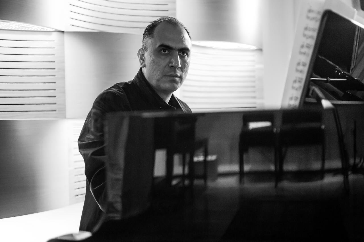 Hombre tocando el piano en una habitación, vista en blanco y negro.