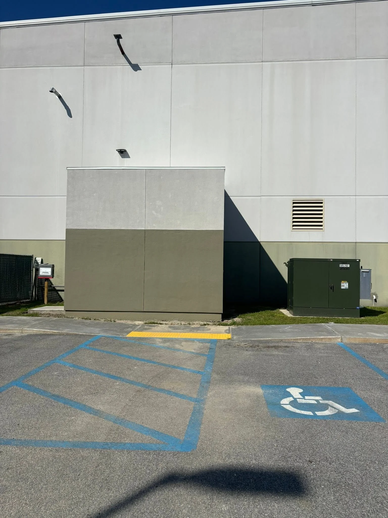 An empty parking lot with blue handicap parking spaces, a green electrical box, a beige building wall, a vent, and parking lot signage.