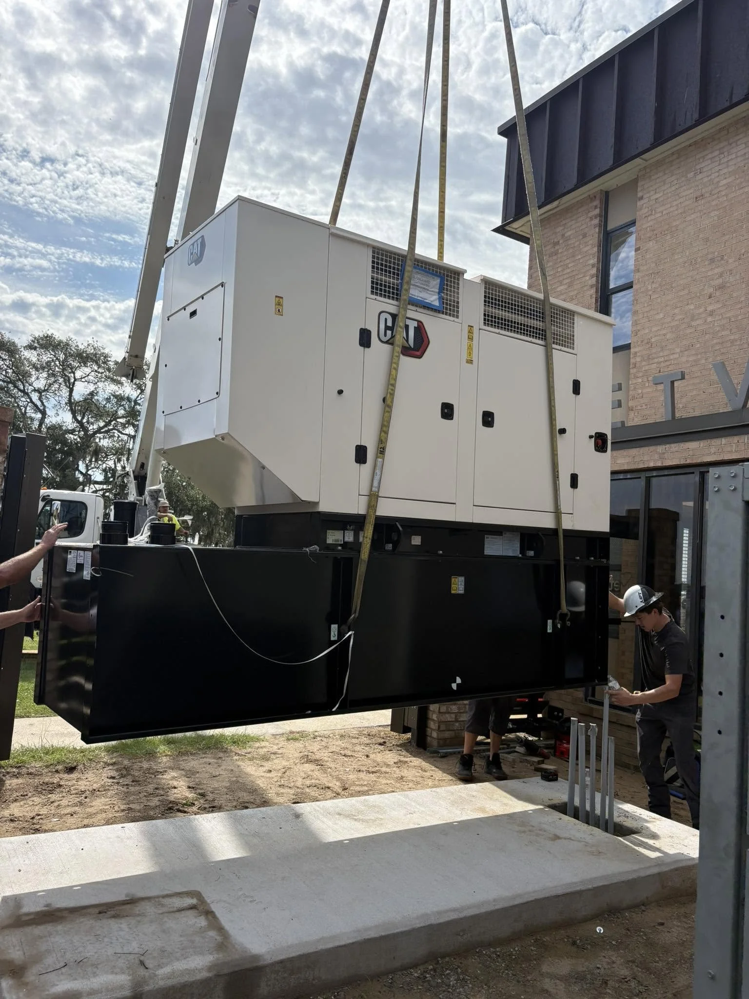 Construction workers installing a large electrical generator outside a building with a brick facade.