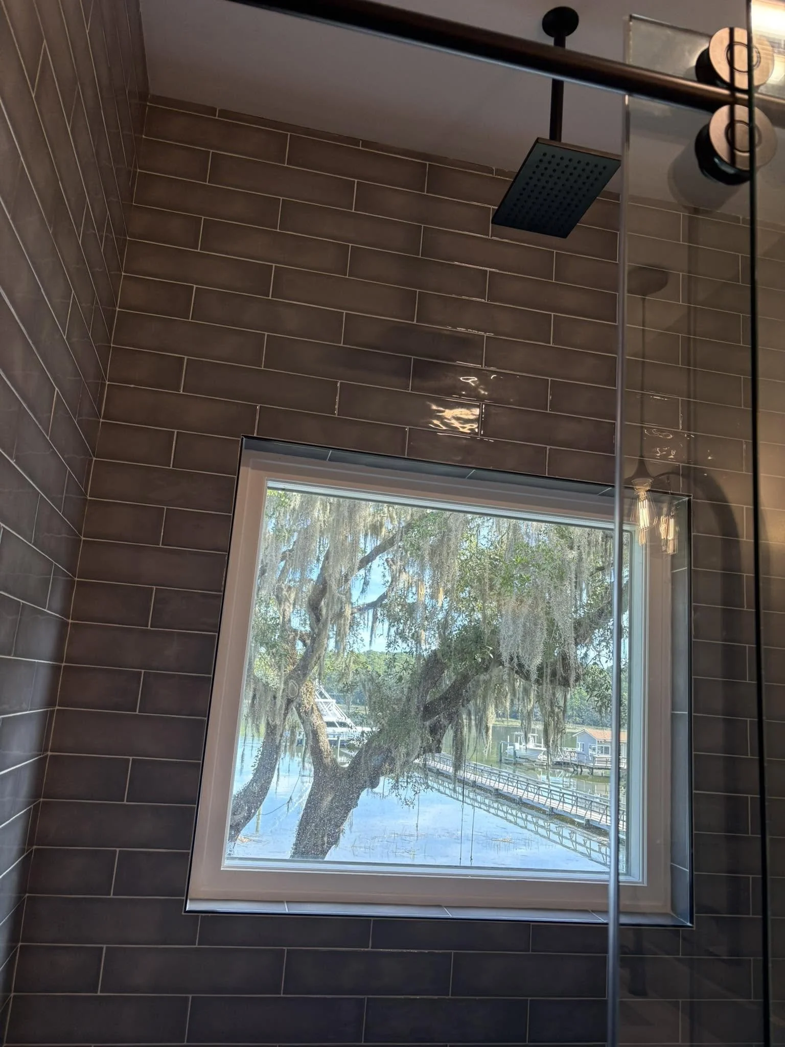 View from a bathroom shower window showing trees and a waterway with boats and docks outside.