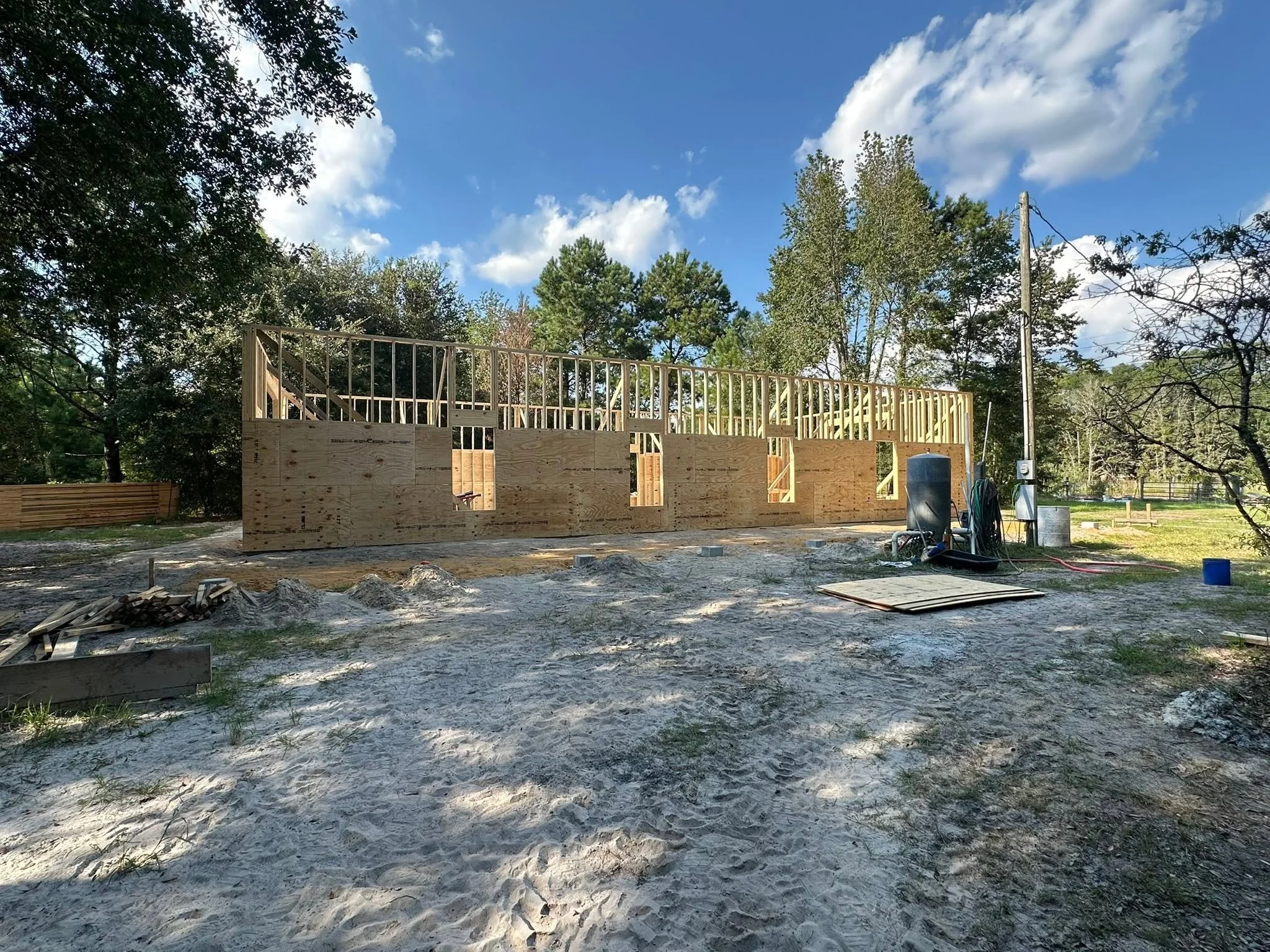 A wooden construction frame of a building under construction, with a blue sky, clouds, and trees in the background.