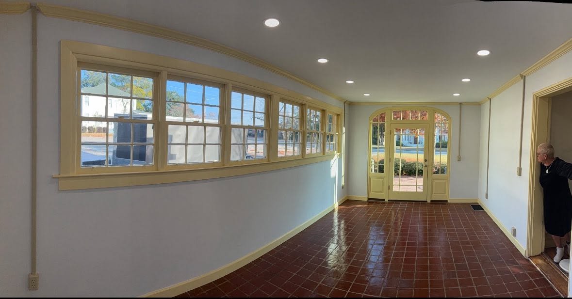 Empty room with large windows, a door, and tile flooring, with a person standing at the doorway.