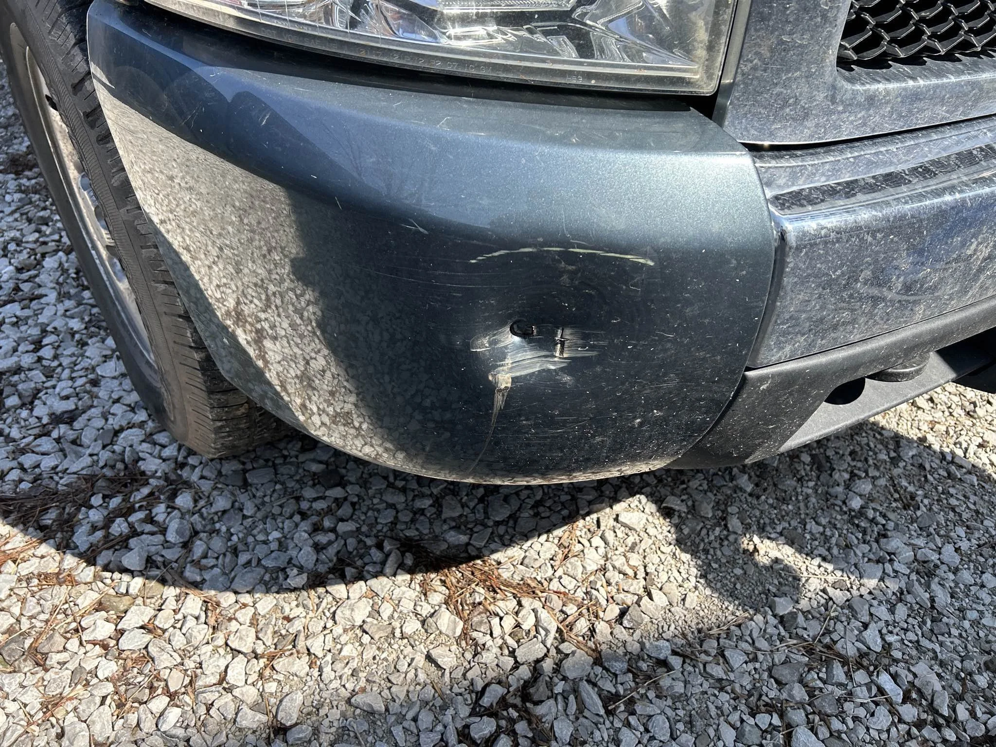 The front right corner of a dark-colored vehicle shows a large scrape and dent on the bumper.